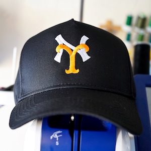 Puede incluir: Una gorra de béisbol negra con un logotipo "NY" bordado en blanco y naranja.