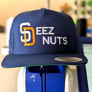 May include: A navy blue baseball cap with a white and orange embroidered logo that says "Deez Nuts".