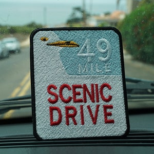 Puede incluir: Un parche bordado blanco y azul con un diseño de gaviota y el texto "49 Mile Scenic Drive".