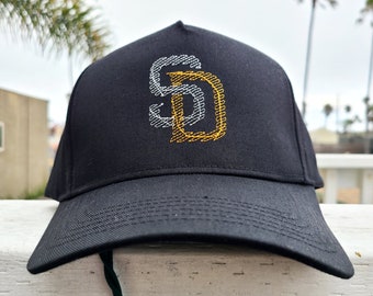 Pode incluir: Um boné de beisebol preto com um logotipo "SD" bordado em branco e dourado.