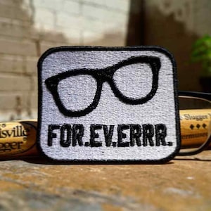 May include: A white embroidered patch with black text and a pair of black glasses. The text reads "FOR.EV.ERRR."