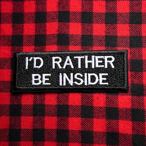 Peut inclure: Patch brodé noir et blanc avec le texte "I'd rather be inside" sur un fond à carreaux rouge et noir.