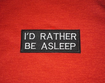 May include: Red hoodie with a black patch that says "I'd rather be asleep" in white text.