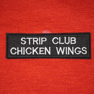 Peut inclure: Patch noir avec du texte blanc qui dit "Strip Club Chicken Wings" sur un fond rouge.
