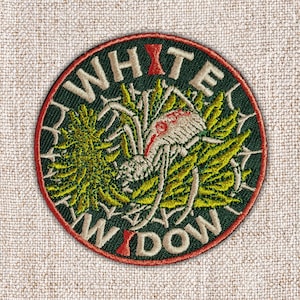May include: Embroidered patch with a dark green background and a red border. The patch features the words "WHITE WIDOW" in a cream-colored font, with a red accent on the letter "T" and "W". A detailed spider and leaves are in the center.