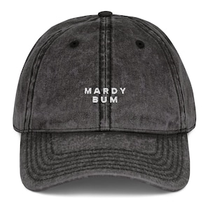 Op de afbeelding: Een antracietkleurige baseballpet met een verwassen look. Op het voorpaneel staat de tekst MARDY BUM geborduurd in witte hoofdletters. De pet heeft een gebogen klep, een knoop aan de bovenkant en gestikte ventilatiegaatjes voor extra lucht.