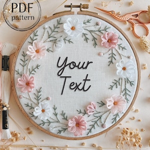 Peut inclure: Un cercle de broderie blanc avec un motif floral rose et blanc. Le cercle a le texte "Your Text" au centre.
