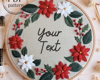 May include: Embroidered hoop art with a wreath of red poinsettia flowers, white flowers, green leaves, and red berries. The center of the hoop says "Your Text".