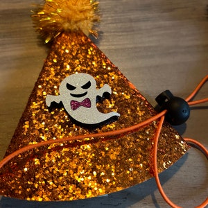 Puede incluir: Sombrero de fiesta de purpurina naranja y dorada con un diseño de fantasma y un pompón amarillo esponjoso en la parte superior. El sombrero tiene una banda elástica para un ajuste seguro.