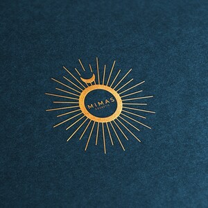 Puede incluir: Logotipo dorado sobre fondo azul oscuro. El logotipo presenta un dise&ntilde;o de sol con una luna creciente y el texto "MIMAS Cosmetic" en un arreglo circular. El dise&ntilde;o es simple y elegante.