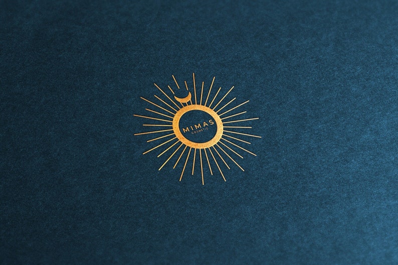 Puede incluir: Logotipo dorado sobre fondo azul oscuro. El logotipo presenta un dise&ntilde;o de sol con una luna creciente y el texto "MIMAS Cosmetic" en un arreglo circular. El dise&ntilde;o es simple y elegante.