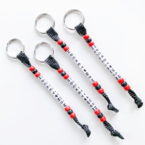 May include: Four black and red beaded keychains with silver key rings. Each keychain has white beads with the text "HOCKEY MOM" on them.