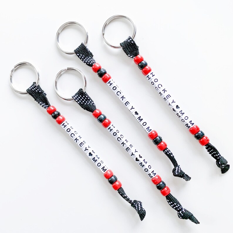 May include: Four black and red beaded keychains with silver key rings. Each keychain has white beads with the text "HOCKEY MOM" on them.