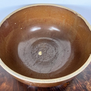 May include: A brown ceramic bowl with a wide rim. The interior of the bowl is a darker shade of brown, with a slightly glossy finish. The rim is a lighter tan color. The bowl is sitting on a wooden surface.