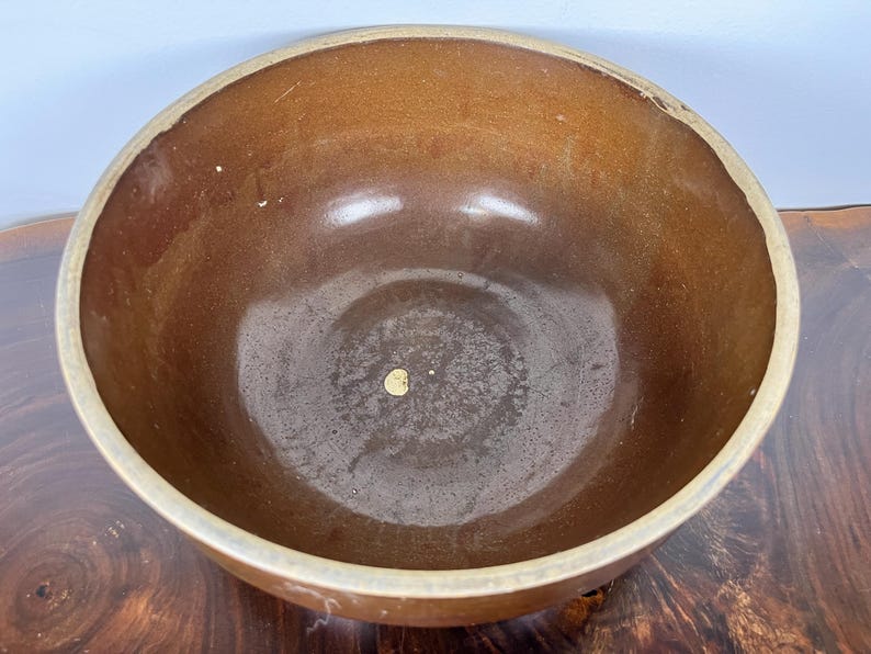 May include: A brown ceramic bowl with a wide rim. The interior of the bowl is a darker shade of brown, with a slightly glossy finish. The rim is a lighter tan color. The bowl is sitting on a wooden surface.