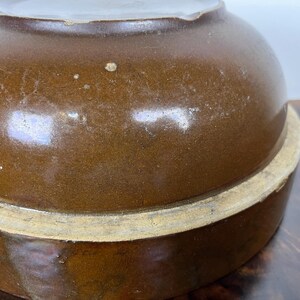 May include: A brown ceramic bowl with a rounded top and a wide base. The bowl has a glossy finish and a light-colored rim. The image shows a close-up of the bowl, highlighting its shape and texture. The bowl appears to be vintage.