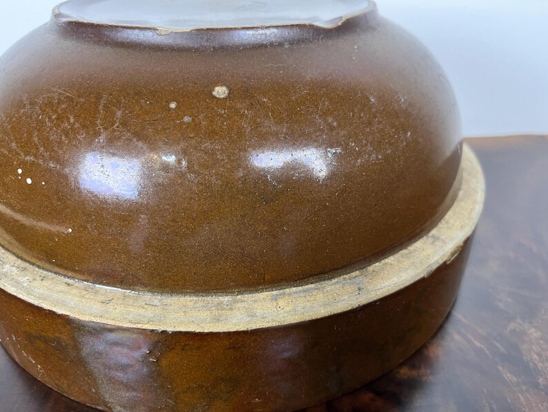 May include: A brown ceramic bowl with a rounded top and a wide base. The bowl has a glossy finish and a light-colored rim. The image shows a close-up of the bowl, highlighting its shape and texture. The bowl appears to be vintage.
