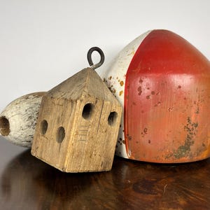 Puede incluir: Una colección de boyas náuticas vintage y un bloque de madera. Las boyas están pintadas de rojo, blanco y naranja. El bloque de madera tiene tres agujeros circulares y un anillo de metal.