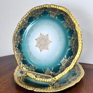 Puede incluir: Juego de dos platos de servir de dos niveles. Los platos tienen una combinación de colores verde azulado y dorado. El plato superior tiene un borde dorado con un borde festoneado y un diseño floral dorado. El plato inferior es verde azulado con un diseño floral dorado y un asa dorada.