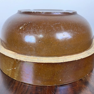 May include: A brown ceramic crock with a rounded top and a wide, cylindrical base. The crock has a glossy finish and a light-colored band around the base. The antique kitchenware is likely used for food storage.