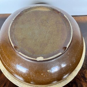 May include: A brown ceramic bowl with a light beige rim. The bowl's interior is a lighter shade of brown, and the exterior has a glossy finish. The bowl is likely used for serving food or as a decorative piece.