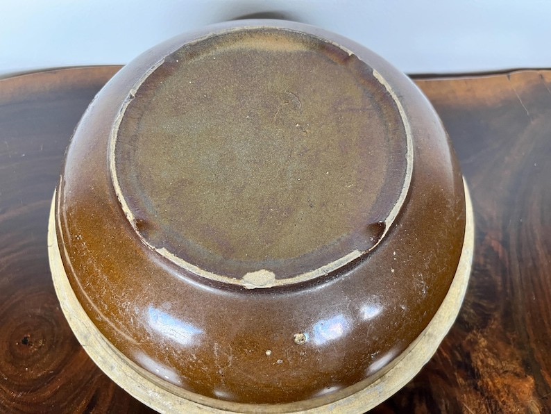 May include: A brown ceramic bowl with a light beige rim. The bowl's interior is a lighter shade of brown, and the exterior has a glossy finish. The bowl is likely used for serving food or as a decorative piece.