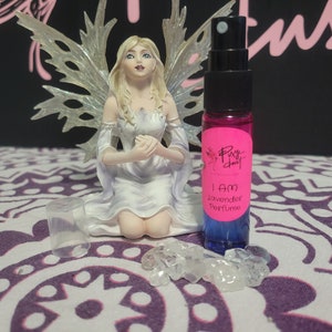 May include: A small bottle of lavender perfume with a pink label that says "I AM Lavender Perfume" and a white fairy figurine in the background.