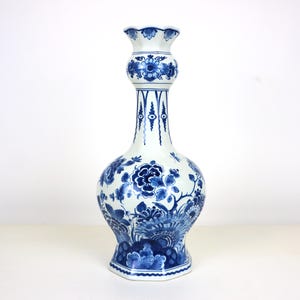 Könnte beinhalten: Eine hohe, weiß-blaue Keramikvase mit bauchigem Boden und schlankem Hals. Die Vase ist mit aufwendigen blauen Blumenmustern verziert. Die Vase hat einen ausgestellten oberen Rand und einen sechseckigen Sockel. Die Vase ist etwa 30 cm hoch.