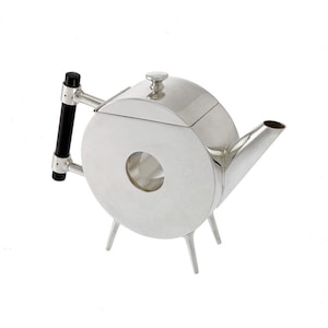 Könnte beinhalten: Eine moderne, silberfarbene Teekanne mit rundem Korpus und schwarzem Griff. Die Teekanne hat einen kleinen Ausguss und steht auf drei dünnen Beinen. Der Griff ist schwarz und silberfarben. Der Deckel ist klein und rund.