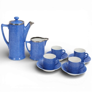 May include: A tea set featuring a tall teapot, a creamer, and four cups with matching saucers. Each piece is finished in a vibrant blue glaze with a dense, white speckled pattern and metallic silver rims on the teapot and creamer.