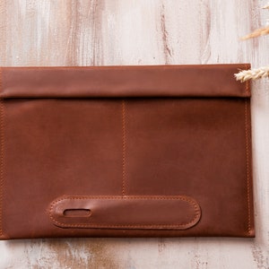May include: A brown leather laptop sleeve with a flap closure and a stitched detail on the front.