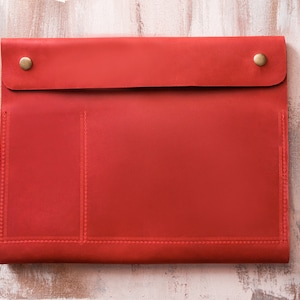 May include: Red leather folder with two pockets and brass accents.