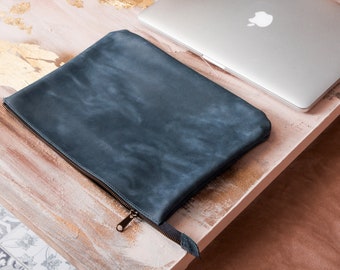 May include: A dark blue leather laptop sleeve with a zipper closure. The sleeve is lying on a wooden surface.