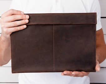 May include: A brown leather envelope clutch with a flap closure and a single stitch down the center.