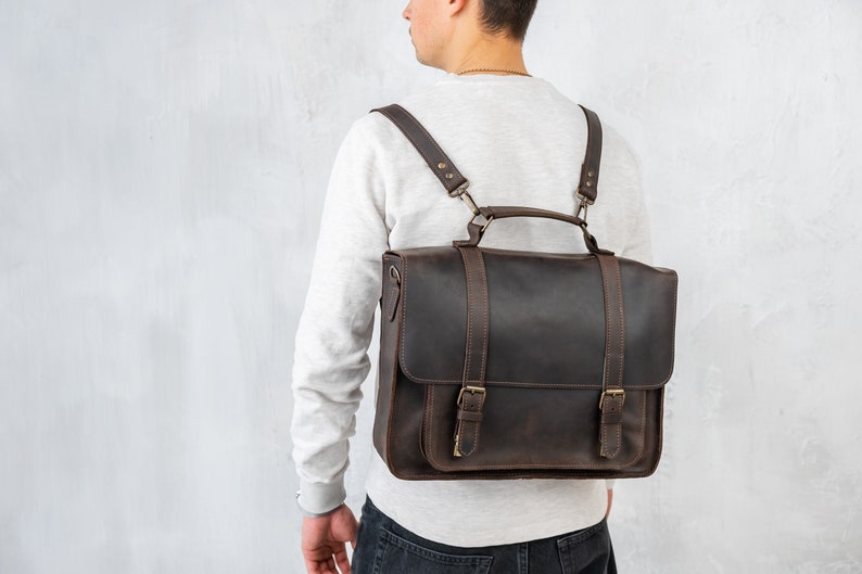 Puede incluir: Un malet&iacute;n de cuero marr&oacute;n con correas ajustables, usado como mochila. La bolsa tiene un asa superior y dos hebillas en la parte delantera.