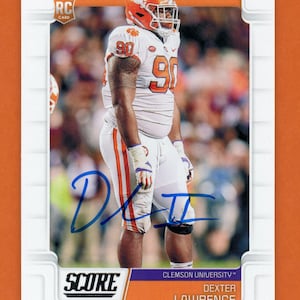 May include: A football trading card featuring Dexter Lawrence in a Clemson Tigers uniform. The card has a white border with the Score logo and the text "ROOKIE RC CARD". Lawrence is wearing an orange helmet and the number 90.