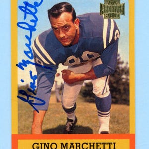 May include: A 2001 Topps Archives trading card featuring a photograph of Gino Marchetti in a blue and white Baltimore Colts uniform. The card includes a blue ink autograph on the left side and the text GINO MARCHETTI BALTIMORE COLTS END.