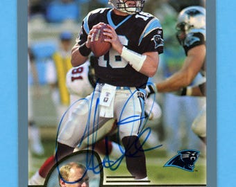 May include: A Topps trading card featuring Chris Weinke, quarterback for the Carolina Panthers, in his team uniform. The card has a blue border and includes an image of Weinke in action, holding a football. The card also features the team logo and Weinke's signature.