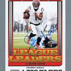 Peut inclure: Carte de football des Bengals de Cincinnati avec Ja'Marr Chase en uniforme blanc à rayures noires, courant avec le ballon. La carte porte le texte "LEAGUE LEADERS" et "1 708 YARDS". La carte est signée à l'encre bleue.