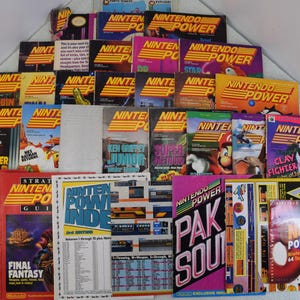 May include: A collection of vintage Nintendo Power magazines, including issues featuring Robin, Super Mario, Clay Fighter, and Final Fantasy. The magazines are in various colors, including red, blue, green, and yellow. The magazines are arranged in a pile, with the covers facing up.