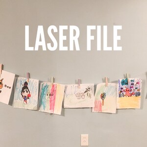 Puede incluir: Una cuerda de dibujos coloridos, incluyendo un unicornio, un monstruo y un gato, están colgados en una pared con pinzas para la ropa. El texto "LASER FILE" está escrito en letras blancas en la pared.