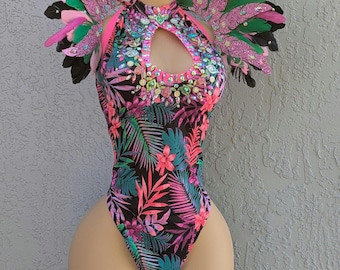 May include: A vibrant, high-neck bodysuit with a tropical floral print in pink, teal, and purple on a black background. The costume features a keyhole cutout and is adorned with sparkling embellishments. Feathered shoulder pieces in pink, green, and black complete the look.