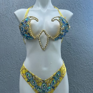May include: Yellow bikini top and bottom with blue and gold embellishments. The top has a plunging neckline and the bottom has a high-cut leg.