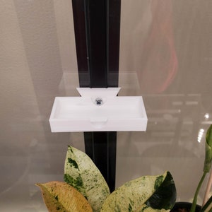 May include: White plastic shelf mounted on a black metal frame. The shelf is designed to hold small items, such as plants or decorations.