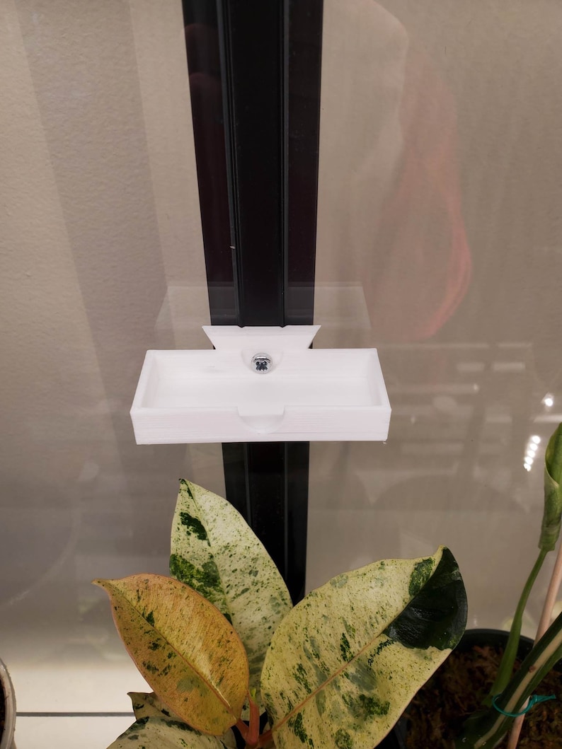 May include: White plastic shelf mounted on a black metal frame. The shelf is designed to hold small items, such as plants or decorations.