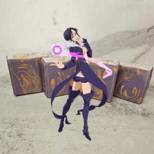 Puede incluir: Cuatro barras rectangulares de jabón con un diseño veteado morado y dorado. Un personaje de anime está superpuesto en la imagen. Las barras de jabón están dispuestas en fila sobre una superficie gris claro.