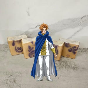 May include: A cartoon character with blond hair wearing a white and gold outfit and a blue cape stands in front of four bars of handmade soap. The soap is a light yellow color with purple swirls.