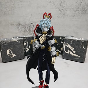 Puede incluir: Un personaje de anime con cabello azul, vistiendo un abrigo negro con detalles rojos, de pie frente a cuatro barras de jabón de mármol negro y blanco.