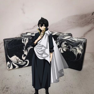 Puede incluir: Una barra de jabón de color blanco y negro con un personaje de una serie de anime de pie frente a ella. El personaje lleva un atuendo blanco y negro con una capa blanca.