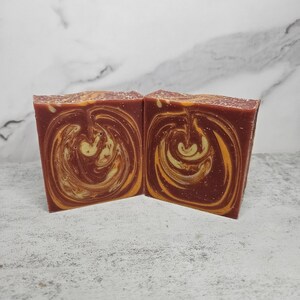 May include: Two bars of handmade soap with a swirl pattern in shades of brown and yellow.